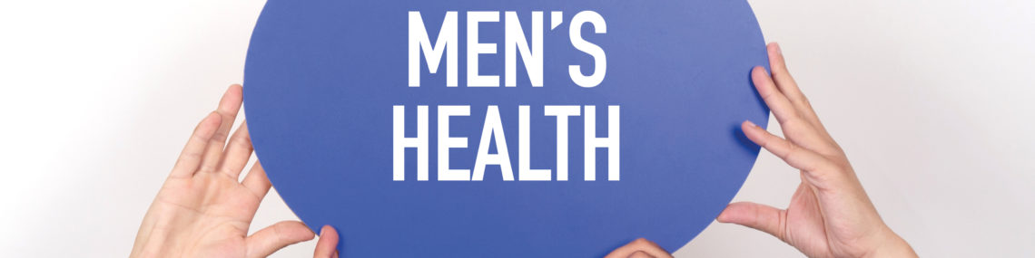 Hands of three men in blue, white, and plaid shirts holding up a blue speech bubble sign with the words “Men’s Health” in white text.