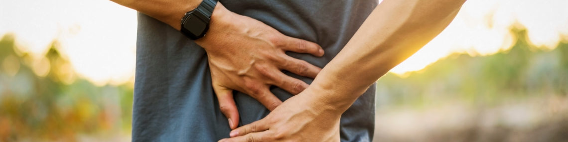 Man outdoors holding lower back and sacrum in pain, symbolising back stiffness and discomfort associated with ankylosing spondylitis (AS).