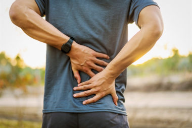 Man outdoors holding lower back and sacrum in pain, symbolising back stiffness and discomfort associated with ankylosing spondylitis (AS).
