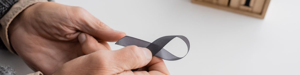 Senior man’s hands holding a grey awareness ribbon, with a blurred wood block calendar showing April 11 in the background, symbolising World Parkinson’s Day.
