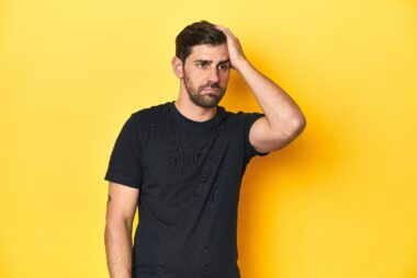Man in black t-shirt against yellow background holding his head with a defeated expression, symbolising the emotional struggles highlighted on R U OK? Day.