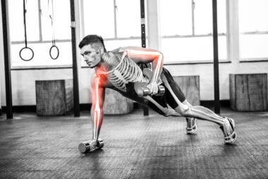Black and white composite image of a muscular man performing single-arm high planks with hand weights, overlaid with a skeleton illustration and red highlights on the humerus bones to symbolise musculoskeletal strain.