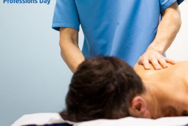 Clinical massage therapist in blue uniform treating a man lying face down on a treatment table.