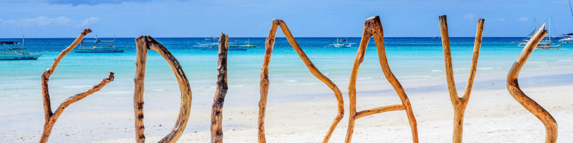 Driftwood spelling out the word “Fridays” on a white sandy beach, creating a relaxed sense of paradise and escape.