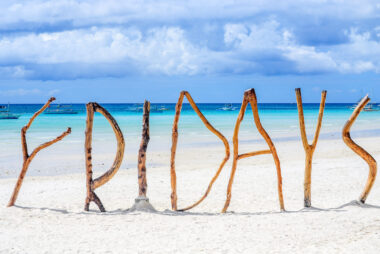 Driftwood spelling out the word “Fridays” on a white sandy beach, creating a relaxed sense of paradise and escape.