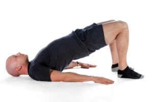 Man performing a Kegel bridge exercise, combining a glute bridge with pelvic floor contraction to strengthen the glutes, lower back, and pelvic floor muscles for urinary control and sexual function.