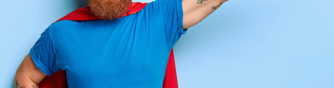Bearded man posing as a superhero character with outstretched arm and clenched fist, smiling confidently.