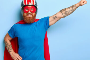 Bearded man posing as a superhero character with outstretched arm and clenched fist, smiling confidently.