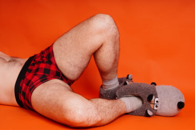 Man lying on his side, shown from the waist down, wearing plaid boxers and plush novelty slippers.