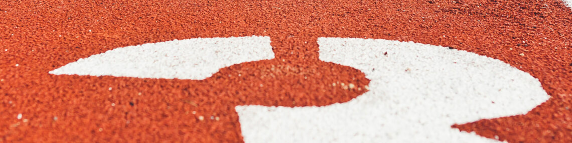 Man wearing blue running shoes in the start position on an athletic track in lane number 3.