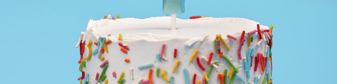 Number four birthday candle burning on a cake with heavy white frosting and multicoloured sprinkles against a light blue background.