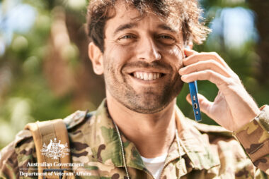 Young male army soldier in uniform talking on a smartphone in a park.