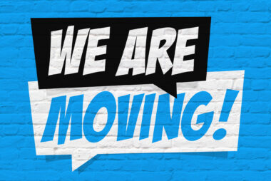 Blue painted brick wall with a black and white speech bubble design containing the words “we are moving!”