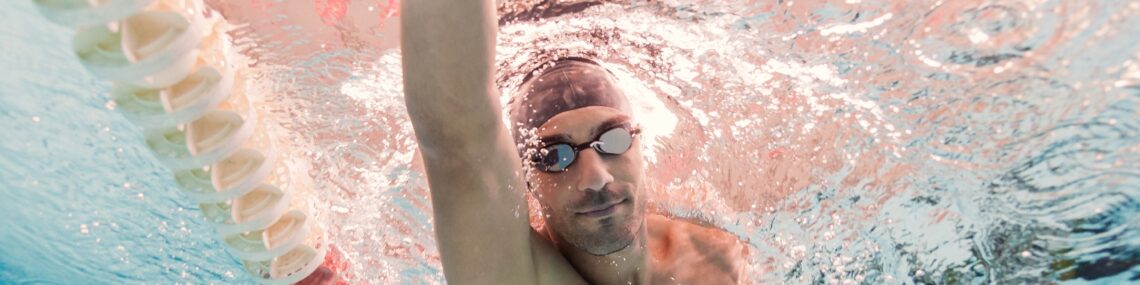 A man swimming freestyle in a pool, with his spine, hips, and arms in rotation — illustrating how swimming supports mobility and spinal health for people with ankylosing spondylitis.