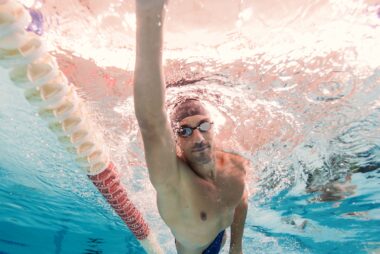 A man swimming freestyle in a pool, with his spine, hips, and arms in rotation — illustrating how swimming supports mobility and spinal health for people with ankylosing spondylitis.